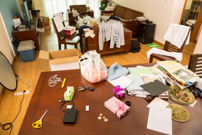 A living room with clothes papers and objects spread across the room